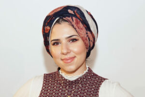 Headshot of Nada Khatib smiling, wearing a black and burgundy headscarf.