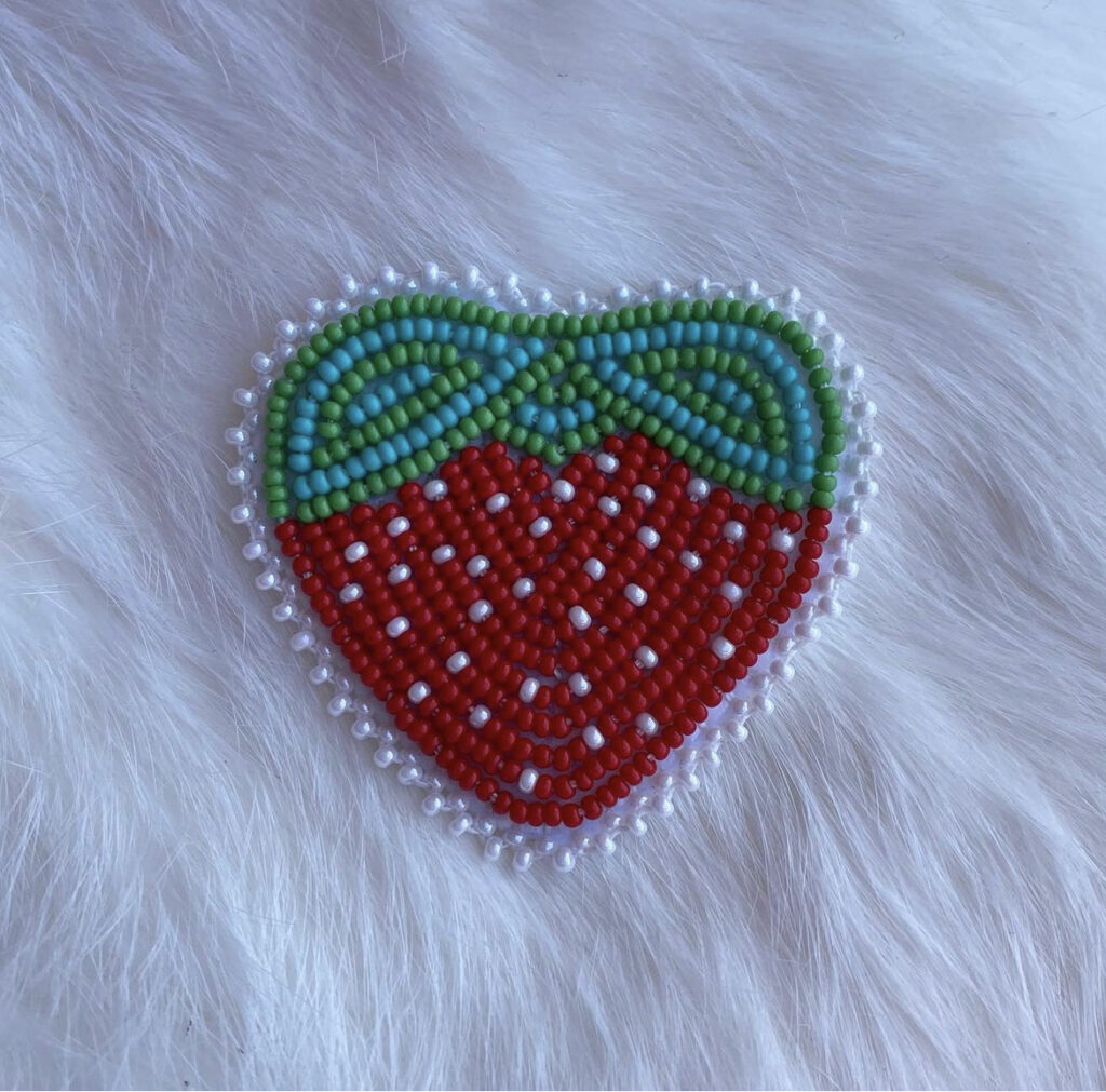 A small beaded strawberry sits on top of white fur.